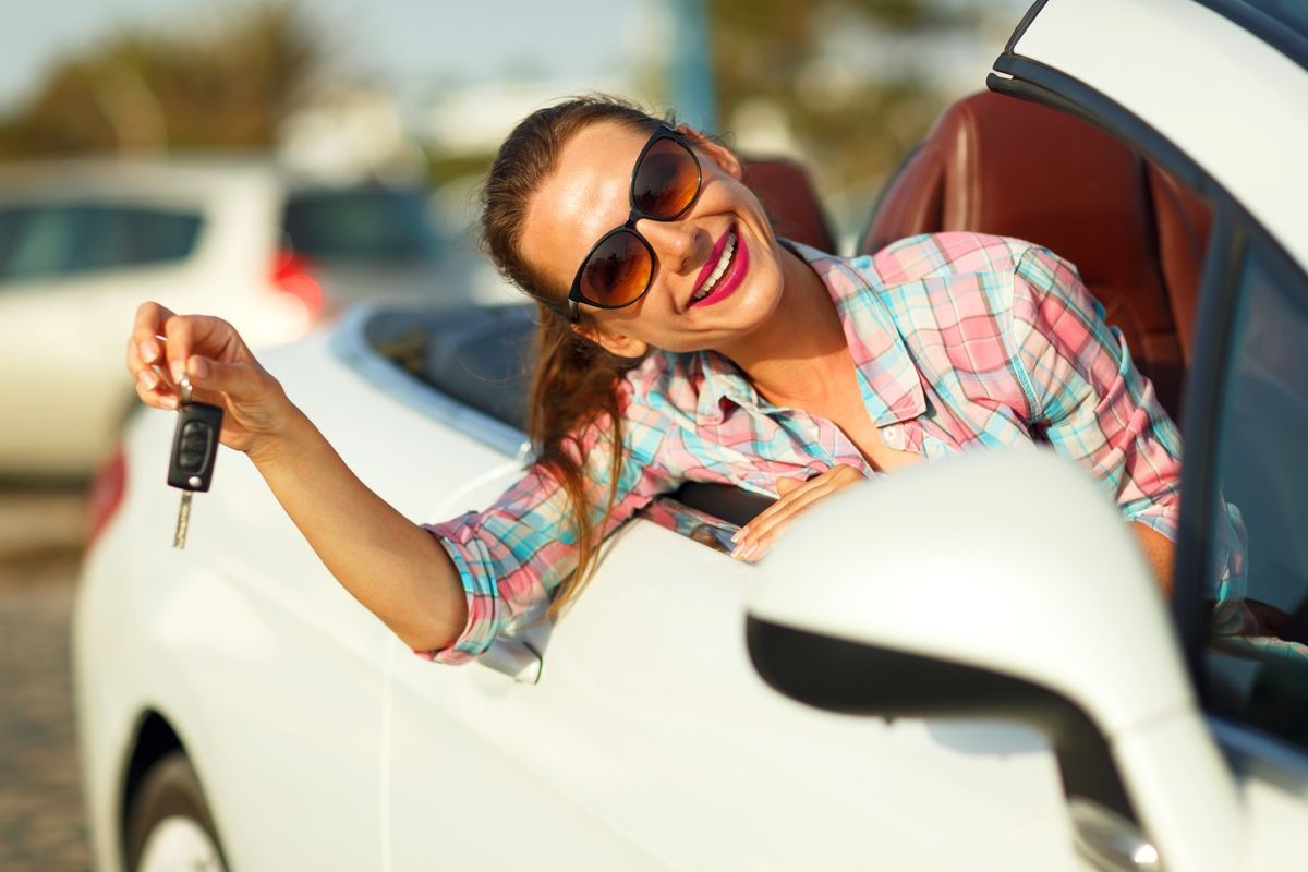 Young pretty woman sitting in a convertible car with the keys in hand - concept of buying a used car or a rental car